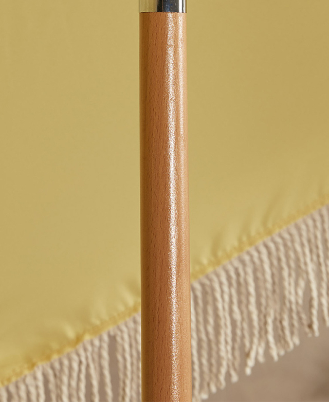 The umbrella base is made from a varnished beech wood. The yellow canopy is in the background. The umbrella base is made from a varnished beech wood. The yellow canopy is in the background.