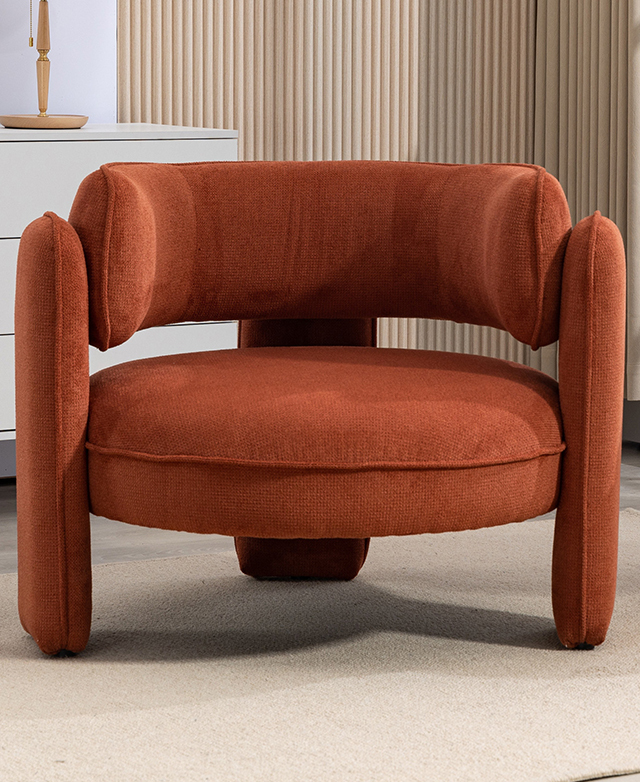 The round-shaped orange armchair is on a stone-coloured rug in front of a beige, fluted wall. The round-shaped orange armchair is on a stone-coloured rug in front of a beige, fluted wall.