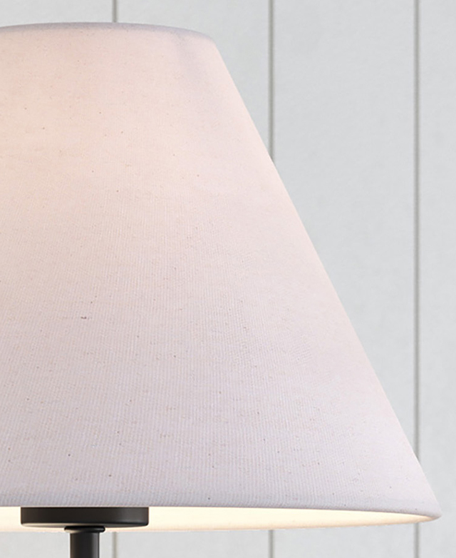 A cropped view of the white fabric tapered lamp shade is illuminated by the hidden bulb. A cropped view of the white fabric tapered lamp shade is illuminated by the hidden bulb.