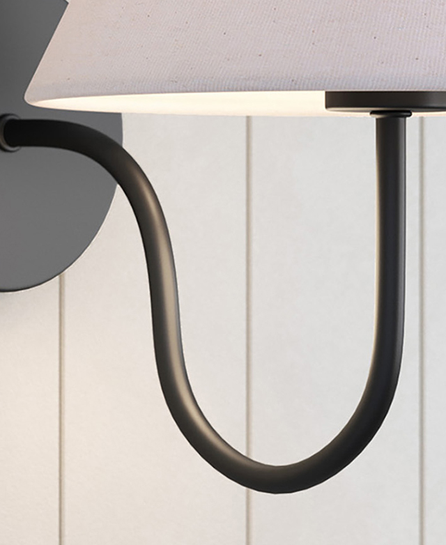 The black steel wall sconce, which has a slender arm and a deep curved, is attached to a panelled white wall. The black steel wall sconce, which has a slender arm and a deep curved, is attached to a panelled white wall.