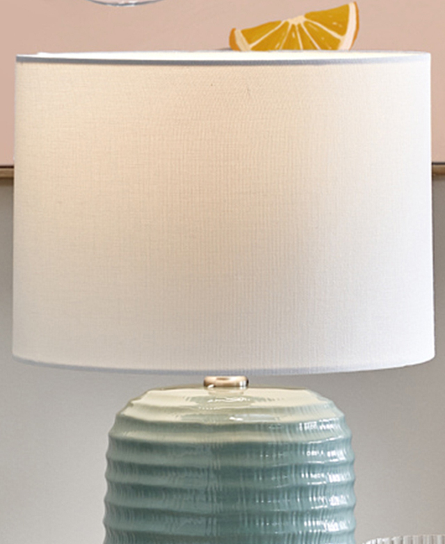 A white fabric drum shade is illuminated by a hidden bulb. A white fabric drum shade is illuminated by a hidden bulb.