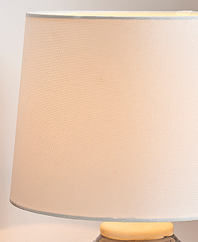 A white fabric drum shade is illuminated by a hidden bulb. A white fabric drum shade is illuminated by a hidden bulb.