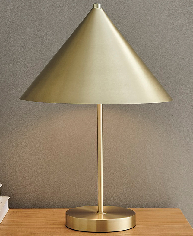 The brass cone-topped lamp is switched on, and it's in front of a white wall on a timber surface.