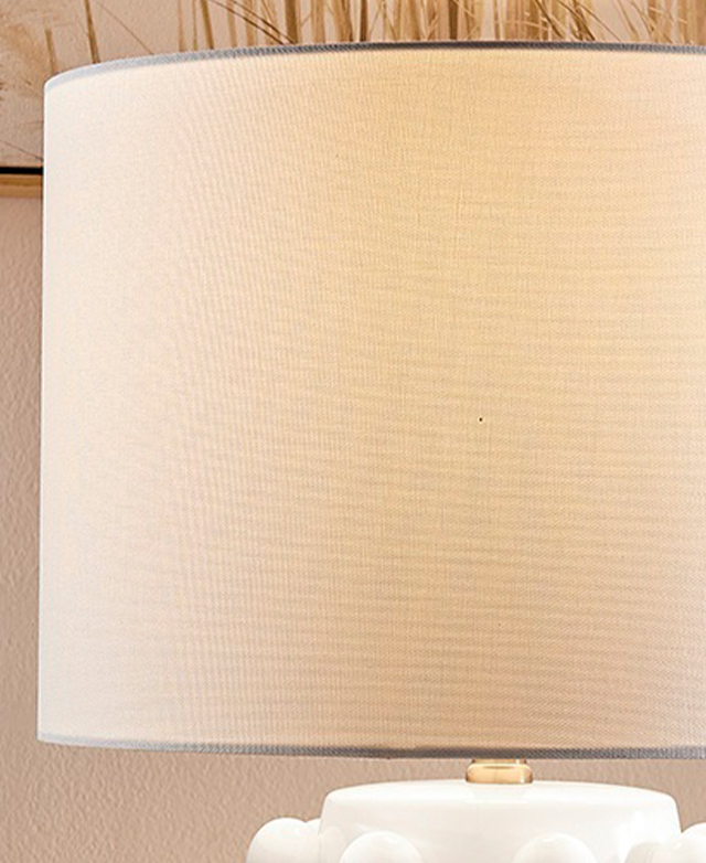 A white fabric drum shade is illuminated by a hidden bulb.