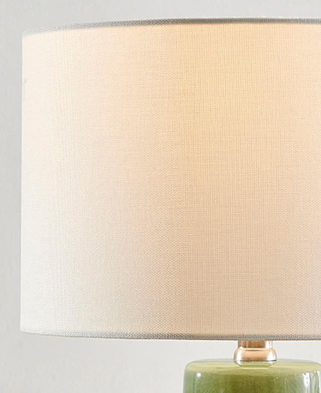 A white fabric drum shade is illuminated by a hidden bulb. A white fabric drum shade is illuminated by a hidden bulb.