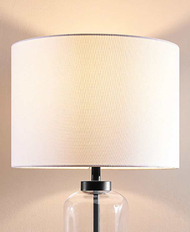 The white fabric drumshade is the focus, with the light turned on. The white fabric drumshade is the focus, with the light turned on.