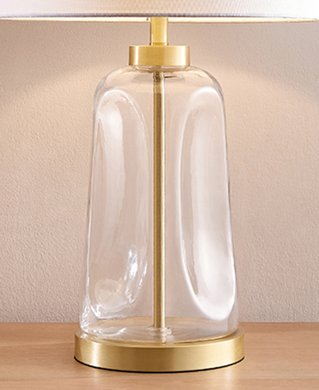 The clear glass lamp base has large dimpled features around it, and the brass elements on the bottom and neck give it polish. The clear glass lamp base has large dimpled features around it, and the brass elements on the bottom and neck give it polish.