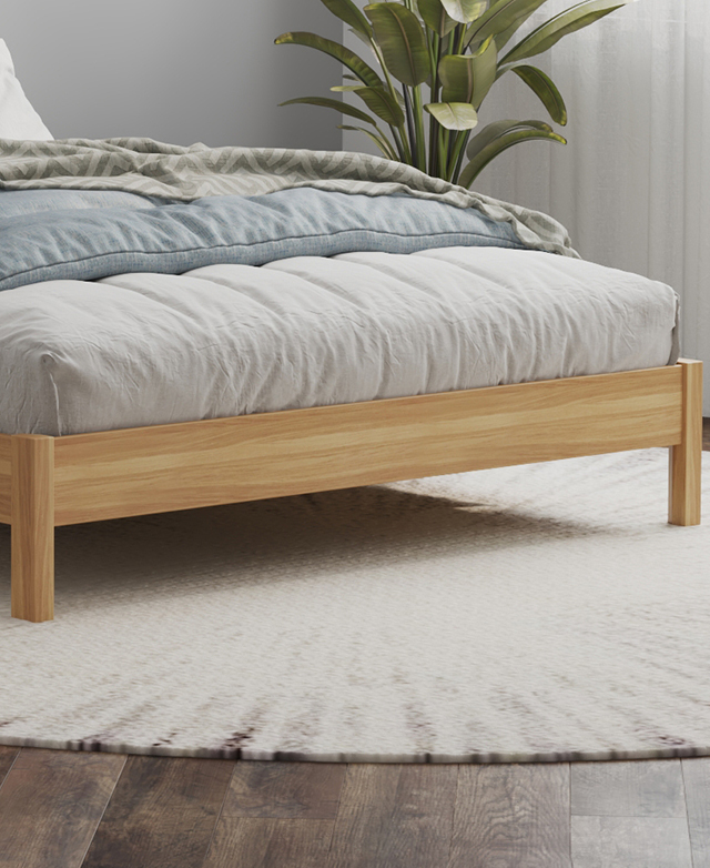 The footend of the bed is positioned on a large round rug, while the bed is dressed in soft grey and blue bedding.