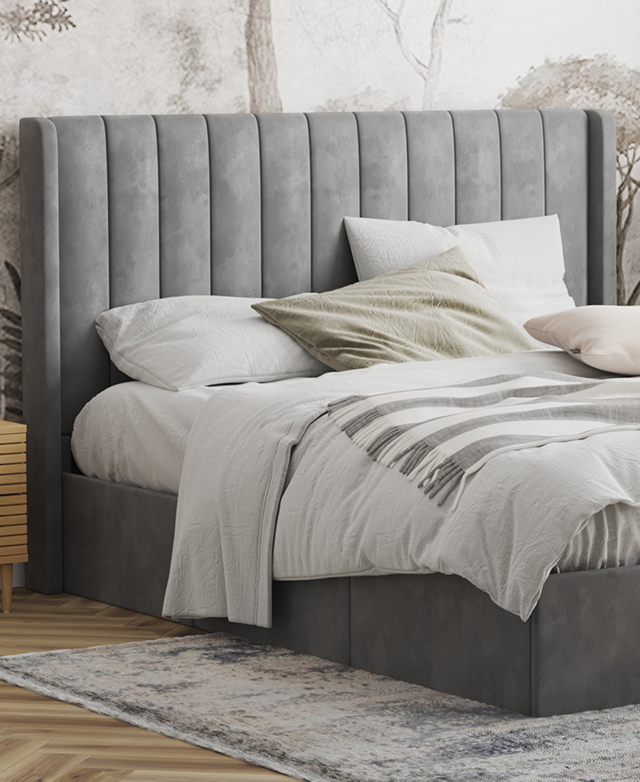 Most of the bed is in the frame; it's dressed in pastel bedding, is in front of abstract wallpaper, and sits atop a blue rug.