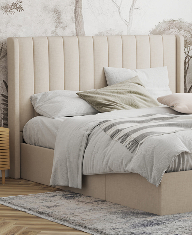 Most of the bed is in the frame; it's dressed in pastel bedding, is in front of abstract wallpaper, and sits atop a blue rug.