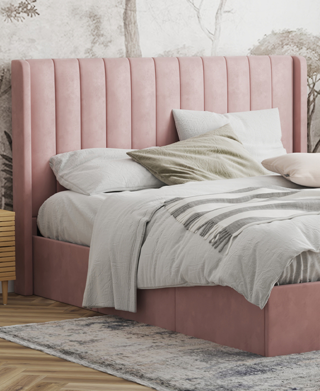 Most of the bed is in the frame; it's dressed in pastel bedding, is in front of abstract wallpaper, and sits atop a blue rug.
