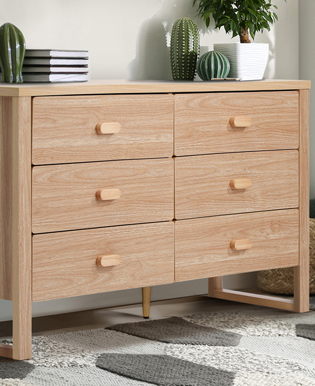 The chest of drawers are on a textured grey and white rug, while on top of the chest are various cacti ceramics and books.