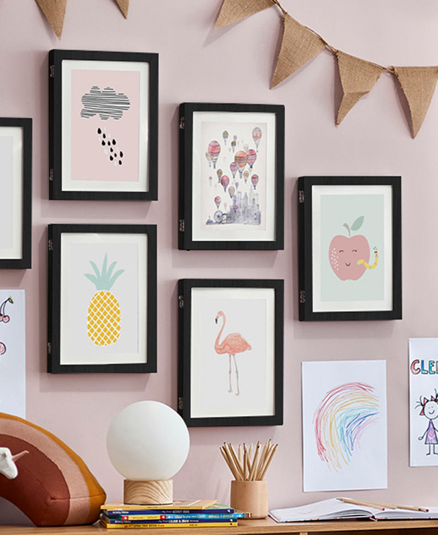 Several colourful black-framed prints are positioned on a pink wall, and framed by hessian bunting.