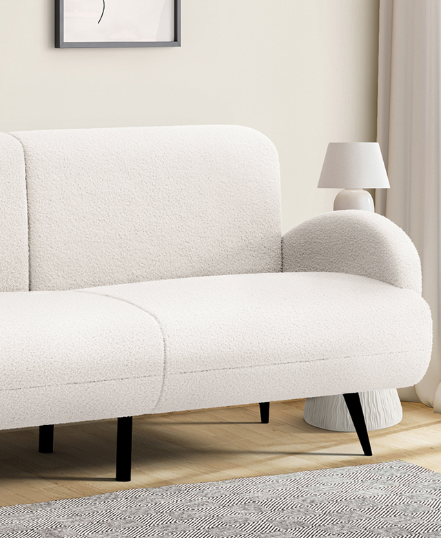The cream sofa is in a cream room on light oak floors; a side table and lamp are next to it, a monochrome rug is in front.