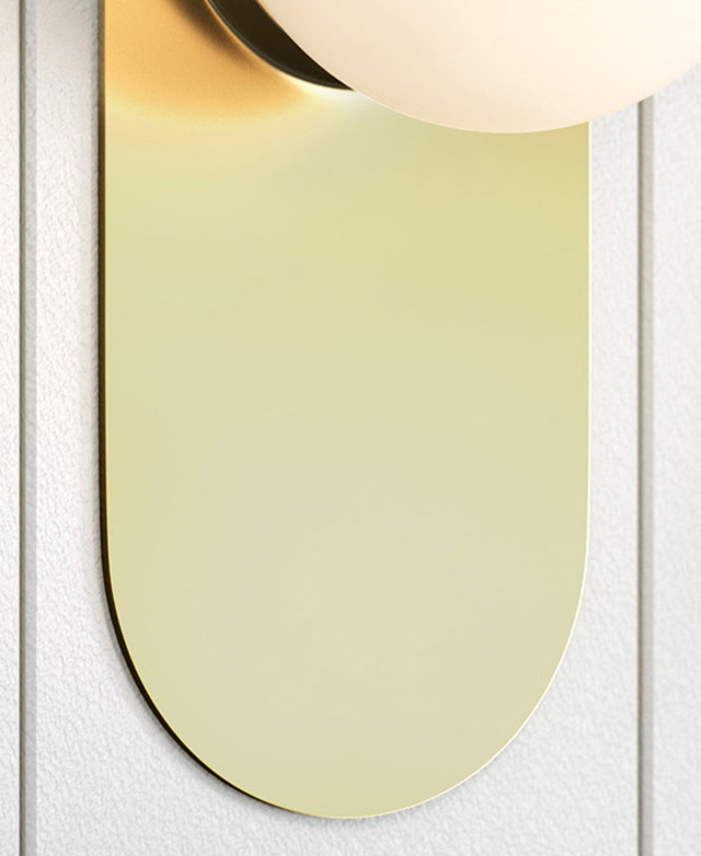 The flat, oval-shaped wall light is golden with a polished finish. It stands out on a matte white wall. The flat, oval-shaped wall light is golden with a polished finish. It stands out on a matte white wall.