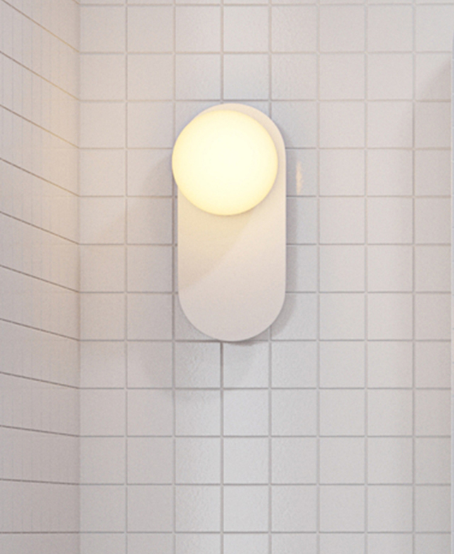The wall light has a translucent, spherical glass shade with a bulb illuminated inside. It's on a white, square-tiled wall. The wall light has a translucent, spherical glass shade with a bulb illuminated inside. It's on a white, square-tiled wall.