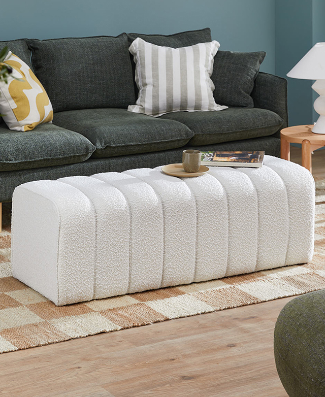 The long creamy ottoman is in front of a green sofa on a taupe & cream checkered rug. A cup, saucer & magazine are on top. The long creamy ottoman is in front of a green sofa on a taupe & cream checkered rug. A cup, saucer & magazine are on top.
