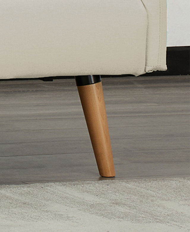 The tapered beech wood leg of a cream sofa is on a timber floor next to a light grey rug. The tapered beech wood leg of a cream sofa is on a timber floor next to a light grey rug.