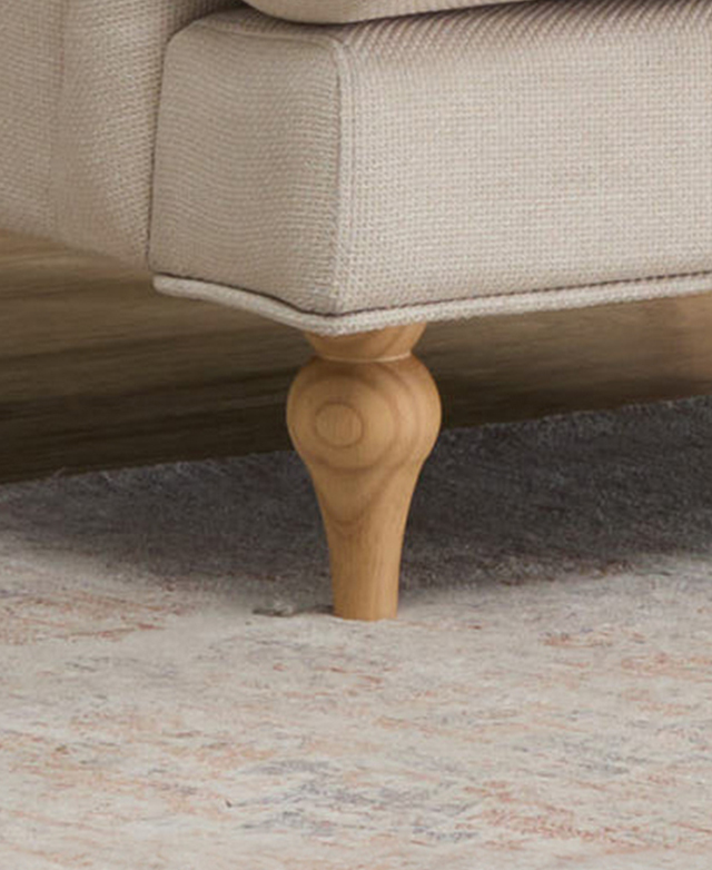 One of the front rubberwood turned legs is in focus. It's on a patterned rug with muted hues. One of the front rubberwood turned legs is in focus. It's on a patterned rug with muted hues.