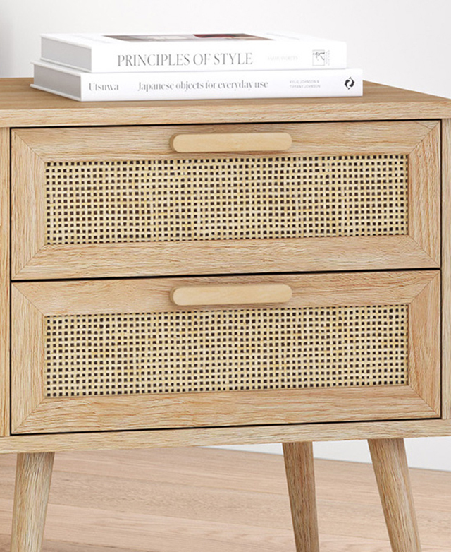 Two books are stacked on top of the side table, which is in a bright room. The woven rattan drawer fronts are the focus.