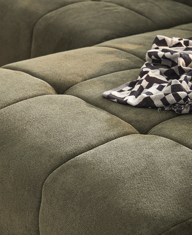 A black and grey blanket is on top of the sofa's large, button-tufted green surface.