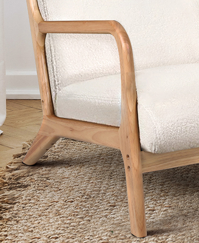 The armchair is on a woven jute rug. The three-quarter angle focuses on the chair's smooth, minimalistic rubberwood frame.