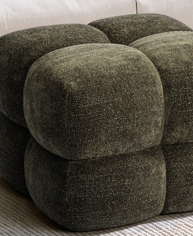 The bubble-like shape of the ottoman is in focus, its rounded edges covered in textured green fabric.