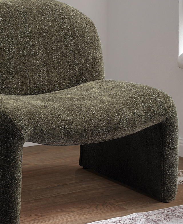 An angled view of the green chair highlights its generous width; it's displayed it on a timber floor near a window.