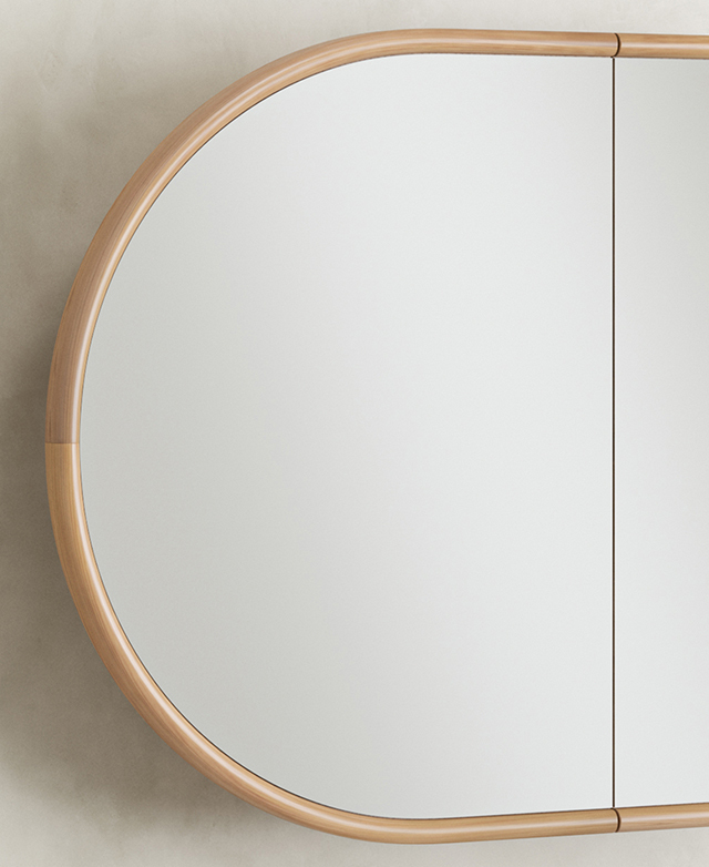 One end of the mirror is in the frame, highlighting its smooth, rounded shape and warm eucalyptus hue.