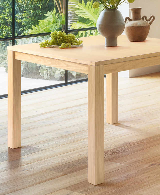 The square table is in a naturally-lit room on timber floors. The dining table has a plate of grapes & ceramic decor on top. The square table is in a naturally-lit room on timber floors. The dining table has a plate of grapes & ceramic decor on top.