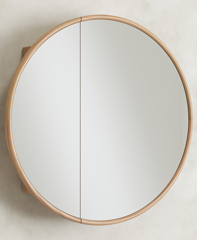 The round, timber-framed mirrored cabinet is positioned on a concrete-look wall.
