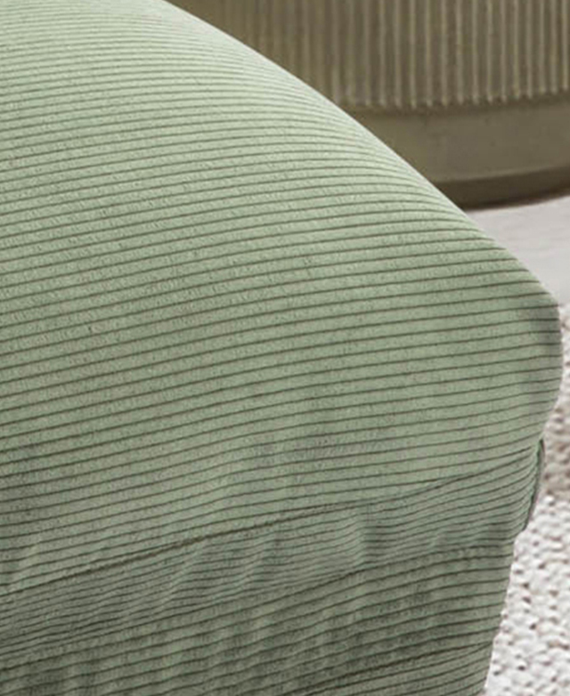 The green sofa bed is zoomed in on to magnify the broad corduroy ridges and its smooth texture.
