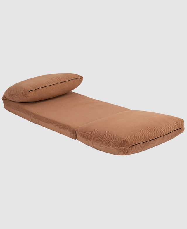 The rust sofa bed is opened flat into a small single bed; the cover's zips are captured at both ends.