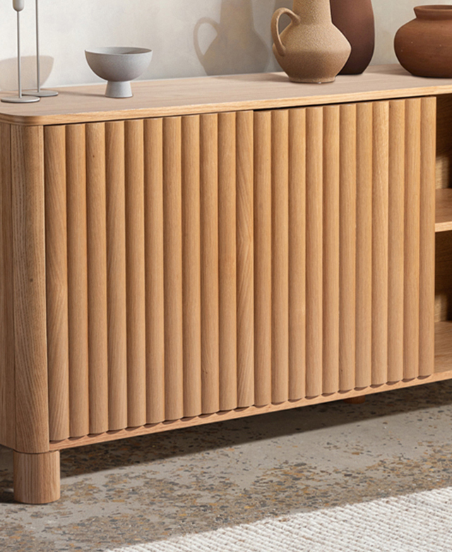 Part of the fluted sideboard is on a concrete floor in front of a white wall, with various earth-toned ceramics on top of it.