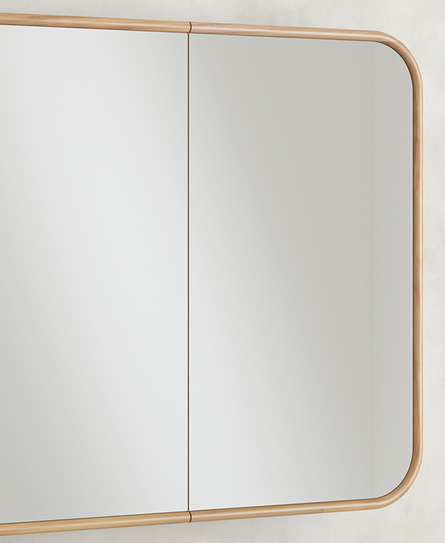 The wide, rectangular, mirrored cabinet is positioned on a concrete-look wall.