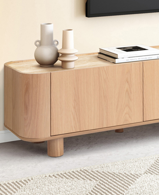 The TV unit is in a bright room on grey flooring. The top surface is styled with ornaments and books, while a TV hangs above. The TV unit is in a bright room on grey flooring. The top surface is styled with ornaments and books, while a TV hangs above.