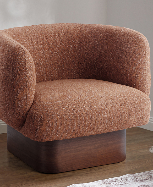The orange and walnut tub chair is in the corner of a brightly-lit room with a patterned rug nearby.