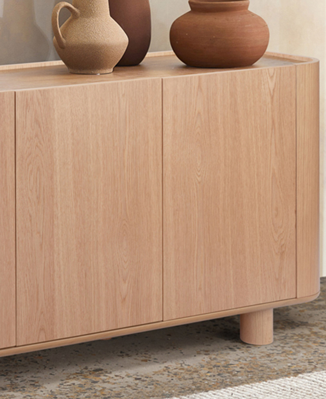 The sideboard is on a concrete floor, and has earthenware on top. The oak grains of the cupboard doors add visual texture. The sideboard is on a concrete floor, and has earthenware on top. The oak grains of the cupboard doors add visual texture.