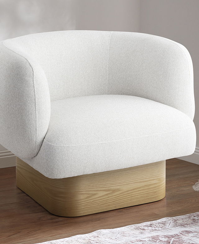 The off-white and oak tub chair is in the corner of a brightly-lit room with a patterned rug nearby.