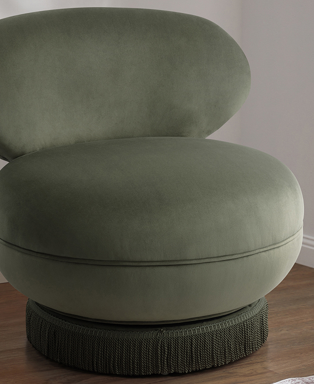 The green velvet swivel chair is shown, its rounded seat, curved backrest, and corded fringing around the base on display.