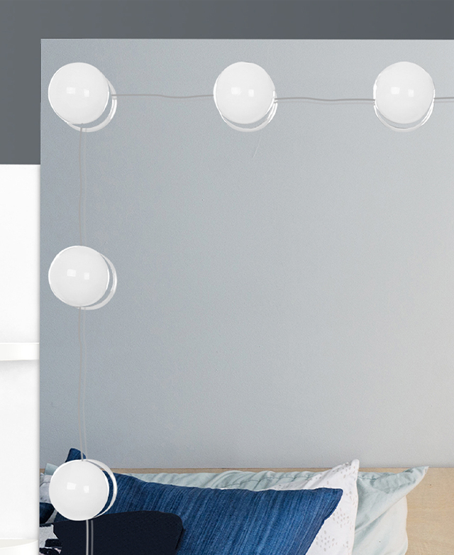 A close-up of the mirror shows the framing LEDs, and pillows on a bed in the reflection.