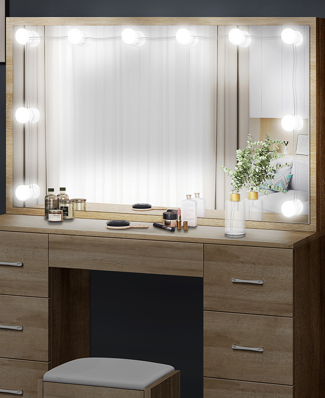 The dressing table's mirror is framed with illuminated LEDs, and beauty items and a bouquet are on the table's surface.