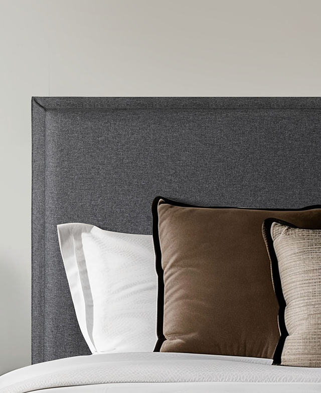 Neutral-toned cushions are piled up in front of the grey upholstered bedhead.