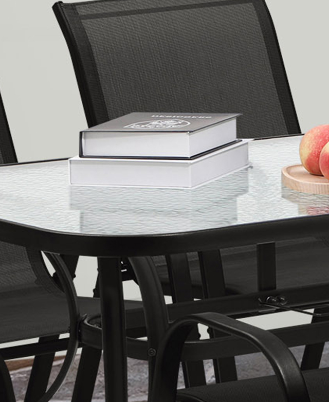 The smooth glass table top has a dimpled-effect and a black metal frame. A stack of books and peaches are on top.