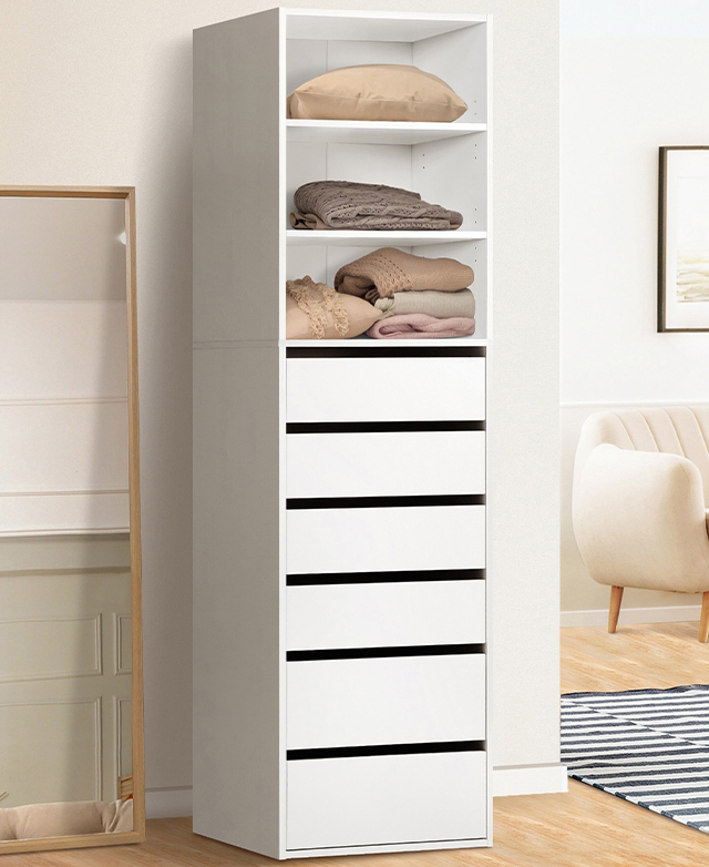 The slender wardrobe unit is filled with various textiles; it's next to a full length mirror in a bright room. The slender wardrobe unit is filled with various textiles; it's next to a full length mirror in a bright room.