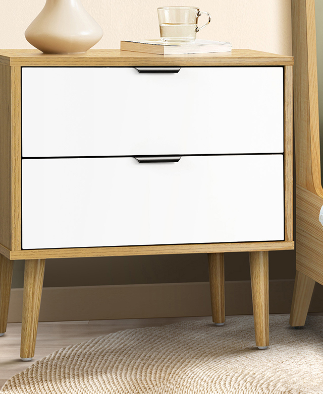 Two-drawer bedside table is positioned next to a just-seen bed; it has a vase, a glass of water, and book on top. Two-drawer bedside table is positioned next to a just-seen bed; it has a vase, a glass of water, and book on top.