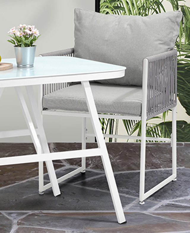 One grey and white armchair is positioned next to the white metal table on grey-toned outdoor tiles. One grey and white armchair is positioned next to the white metal table on grey-toned outdoor tiles.