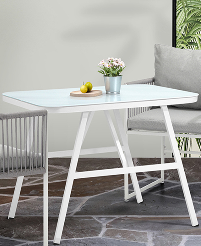 Fruit and a pot of flowers are on top of the table's glass surface, and two chairs are positioned next to the table. Fruit and a pot of flowers are on top of the table's glass surface, and two chairs are positioned next to the table.