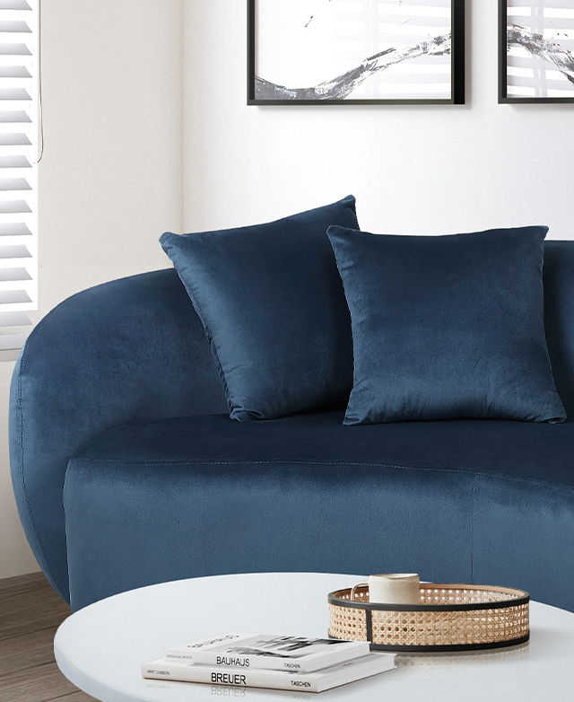 A blue sofa is positioned in a white, bright living room; artwork is on the wall behind, and a coffee table is in front.