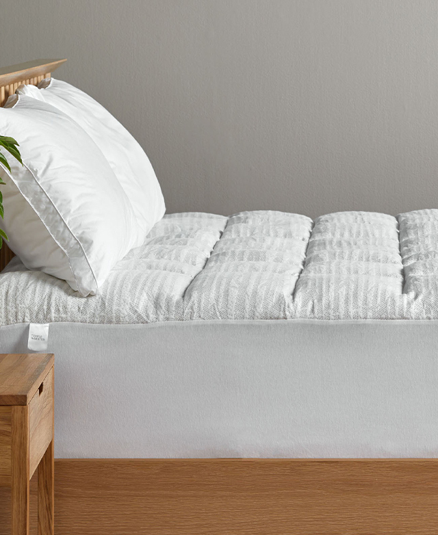 A side view of the mattress topper fitted on to a deep mattress. Two pillows are on top.